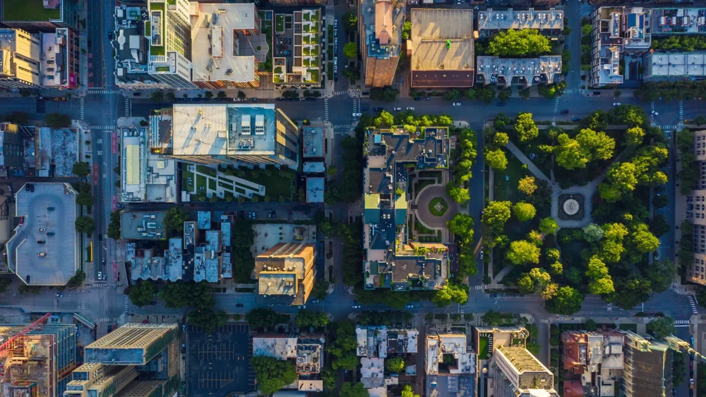 Aerial view of a city block showcasing thoughtful cities planning, with well-organized buildings, streets, parked cars, and a green park filled with trees and walking paths.