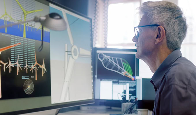 A person analyzes wind turbine designs on multiple computer screens in an office setting.