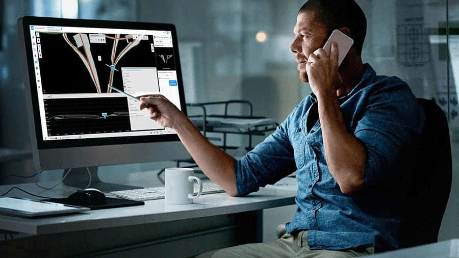 A man sits at a desk talking on a phone while pointing at a computer screen displaying engineering design software, reviewing a COPEL Distribuição case study.